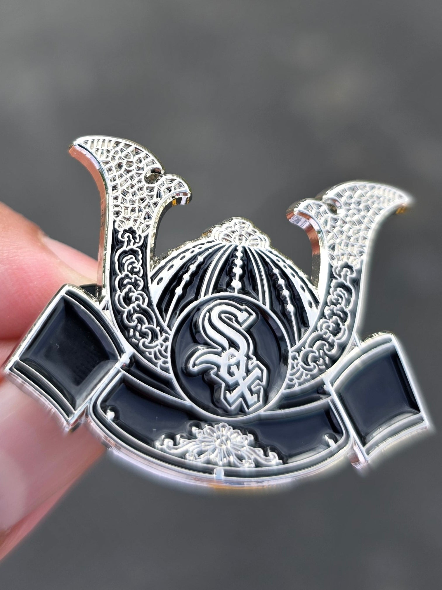 A silver Samurai Kabuto hat pin with black enamel details